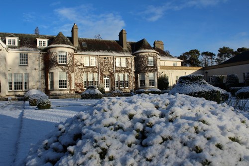 Front view of Rufflets St Andrews in winter with snow-covered shrubs and a bright blue sky.