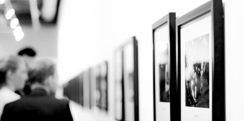 Visitors viewing framed photographs in a contemporary art gallery with a minimal white interior.