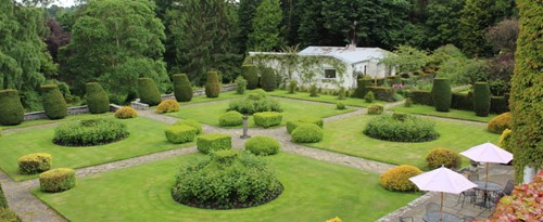 Symmetrical formal garden with neatly clipped hedges and green lawns viewed from above.
