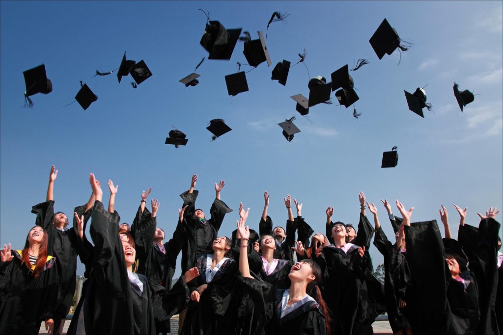 Graduates in black robes tossing their caps into the air under a bright blue sky promoting the Rufflets' graduate event venue in St Andrews.