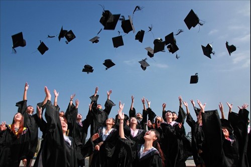 Group of graduates throwing mortarboards into the air under a clear blue sky.