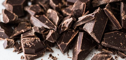 Pile of broken dark chocolate pieces with sharp edges on a white surface.