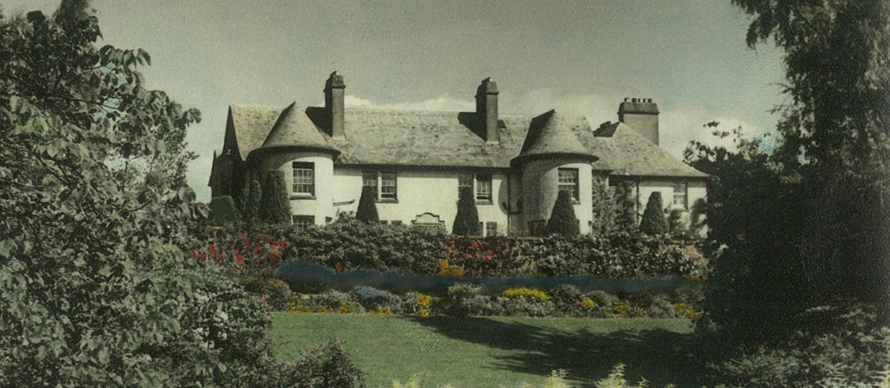 Vintage photo of the grand white mansion of Rufflets hotel in St Andrews with conical towers and lush, colourful garden landscaping.