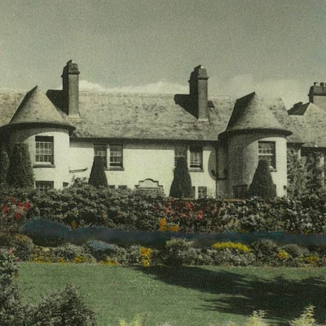 Vintage photo of the grand white mansion of Rufflets hotel in St Andrews with conical towers and lush, colourful garden landscaping.
