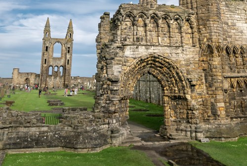 Stone ruins of St Andrews Cathedral with pointed towers and archways under a blue sky.